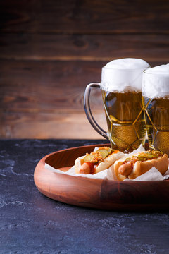 Photo of two glasses of beer and hot dogs on wooden tray