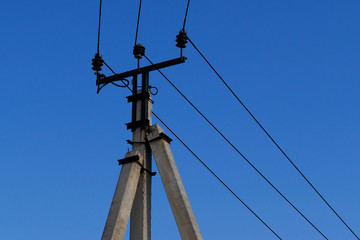 Support line with electrical wires with black porcelain insulators against a clear blue sky.