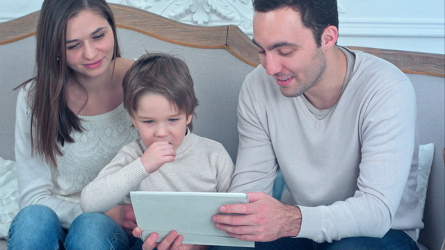 Dad, mom and their young son having fun by playing together with a tablet sitting on a couch