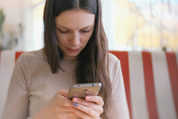 Young beautiful woman brunette typing and sending message in her mobile phone in cafe and waiting her friends.