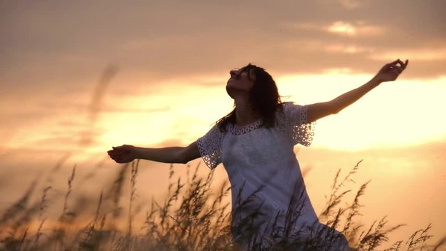 Beautiful girl wearing white dress running through beautiful field at sunset. Young woman jogging at the meadow and enjoying freedom. Summer leisure at nature concept.