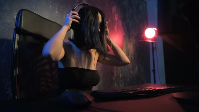 Woman starts online game with her freinds. Gamer girl playing online game on a pc computer wearing headset and talking with a team using microphone