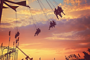 people riding rides and enjoying the summer atmosphere at a state fair at dusk toned with a retro vintage filter app or action - obrazy, fototapety, plakaty