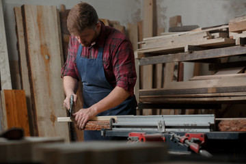 Master carpenter saws board with hacksaw in workshop