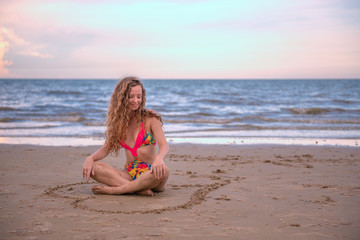 Fototapeta na wymiar Portrait happy woman sitting in the Heart shape drawing on the sand at the beach with enjoying and refreshing, summer beach relaxing time concept.