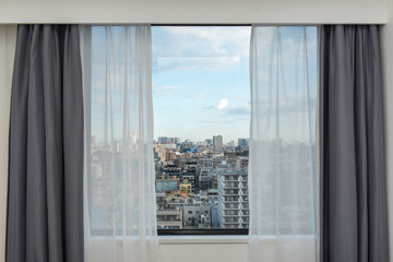 Fototapeta na wymiar Beautiful view from the bedroom with window curtains and cityscape, blue sky, modern home decor.