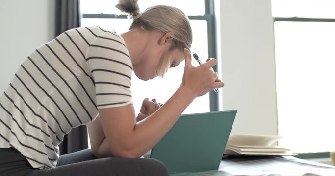 Young woman studying, reading, writing, drawing, relaxing on bed in apartment or dorm