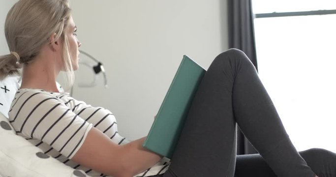 Young woman studying, reading, writing, drawing, relaxing on bed in apartment or dorm
