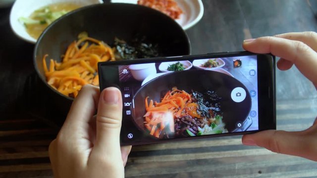 Taking Food Photo of Traditional Korean Dish Bibimbap Served Along With Small Side Dishes Clled Banchan on Mobile Phone. Asian Authentic Cuisine
