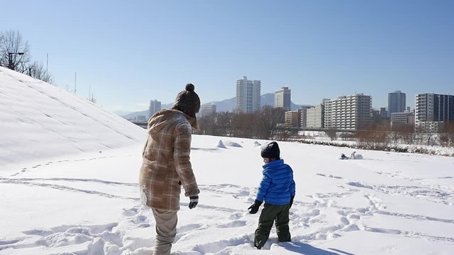 Asian mother and her son playing snow together in the park , sapporo japan slow motion 