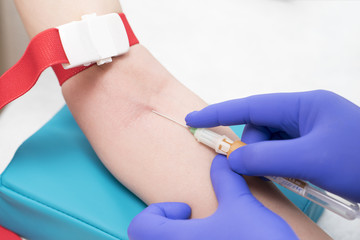 Obraz premium caucasian nurse with blue latex glowes is taking blood for analysis or research from patient vein to plastick vial