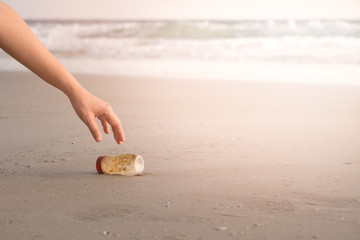 The hand of a woman is picking up a plastic bottle to clean the beach