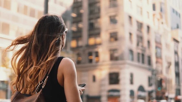 Young beautiful woman walking in downtown of New York, America, looking around and using smartphone.
