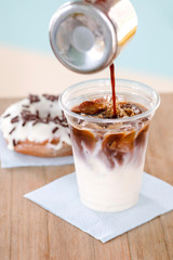 Close-up shot of delicious fresh coffee filling plastic cup with cold milk and ice cream on table in donut cafe