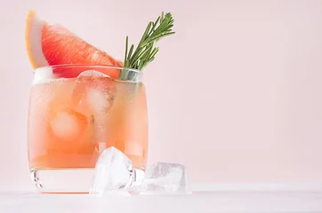 Zelfklevend Fotobehang Summer fresh homemade grapefruit lemonade with ice cubes and rosemary on light pink background. © finepoints