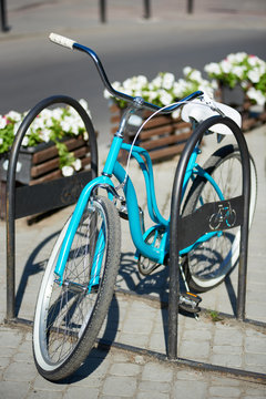Close-up of blue vintage bicycle at street parking outdoors. On a blurry background of guilt, flower beds with flowers. Sunny day