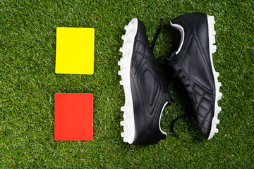 two penalty cards for the referee and soccer shoes, against the background of grass