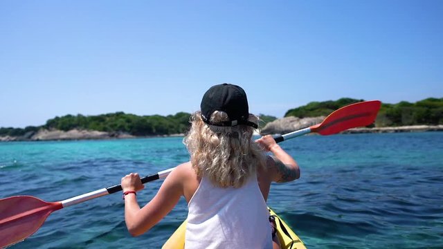 Woman paddling on crystal clear water in boat next to shore in slow motion