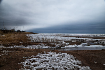 landscape with frozen sea, sandy beach and dry grass on it
