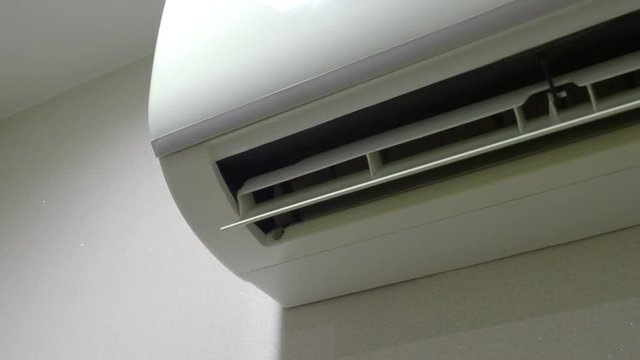 Air Conditioner on the wall is working which wind blade moving and swinging to provide cool wind to hot empty room but it may cause of global warming in the future.