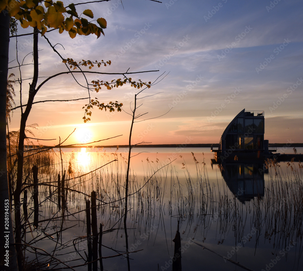 Wall mural Sonnenuntergang am Geierswalder See mit Zweigen im Vordergrund und den Silhouetten zweier schwimmender Häuser