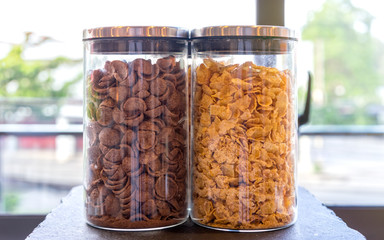 Chocolate and corn flakes breakfast cereal in transparent glass jars, selective focus with shallow...