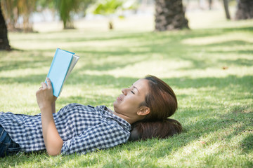 woman enjoy listening music on-line and reading book under the tree in park