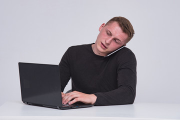 Portrait of a cute young guy with a laptop on a white background with a smartphone.