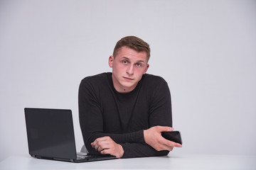 Portrait of a cute young guy with a laptop on a white background with a smartphone.
