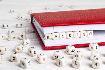 Word Hacking written in wooden blocks in red notebook on white wooden table.