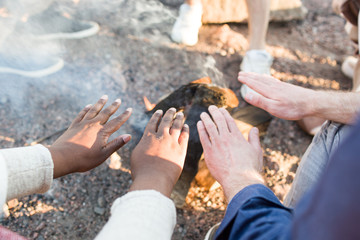 Crop multiracial people warming hands near fire during nice beach party. 