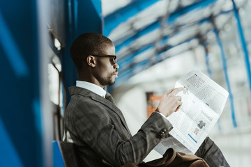 African american businessman wearing suit reading newspaper on bench