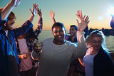 Young African-American woman with glass of cold beverage smiling and looking at camera while dancing among diverse friends on nice party. 