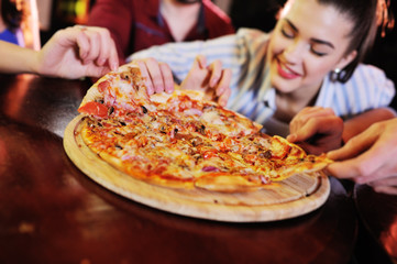 A group of friends eat pizza at a bar or pizzeria.