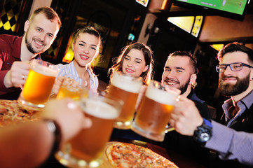 happy cheerful friends drink draft beer and clink glasses in a bar or pub