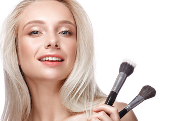 Beautiful young girl with a light natural make-up,brushes for cosmetics and nude manicure. Beauty face. Picture taken in the studio on a white background.