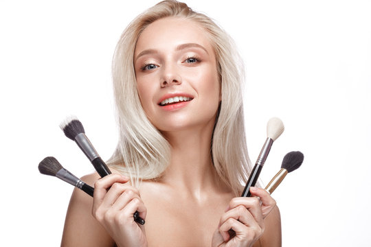 Beautiful young girl with a light natural make-up,brushes for cosmetics and nude manicure. Beauty face. Picture taken in the studio on a white background.