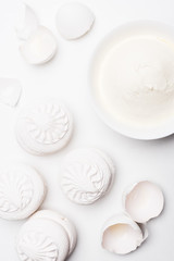 top view of delicious zefir with bowl of sour cream and cracked egg shells on white surface