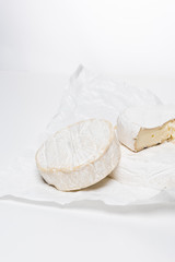 close-up shot of tasty brie cheese on crumpled paper and on white surface