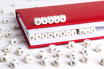 Father's Day greeting message written in wooden blocks in red notebook on white wooden table.