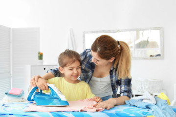 Fototapeta premium Housewife with daughter ironing clothes in laundry room