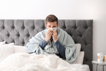 Sick young man with tissue suffering from cold in bed