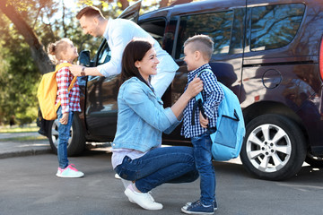Young parents saying goodbye to their little children near school