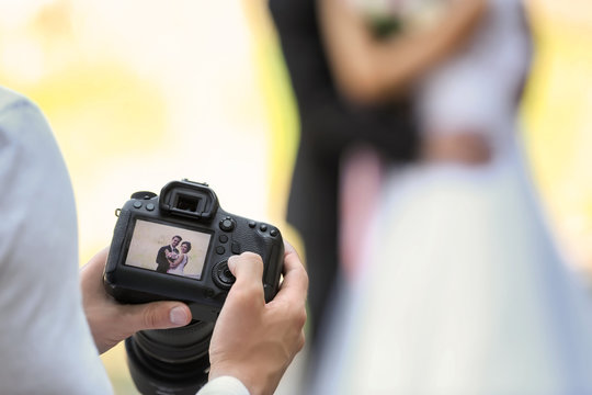 Professional photographer with camera and wedding couple, outdoors