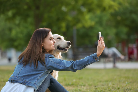 Young woman taking selfie together with her dog in park. Pet care