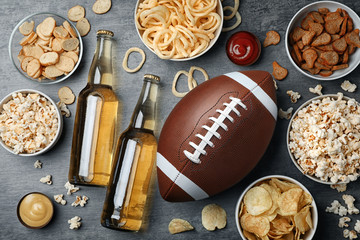 Table full of tasty snacks and beer prepared for watching American football on TV, top view