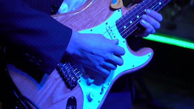  The guitar player is very active on stage with his rock band.  close-up,  flashing light