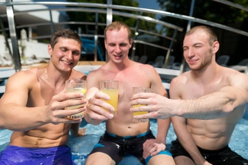 celebration, party, vacation concept. on the nosing of swimming pool that placed outdoor under the sky there is a company of three young and strong man who are clinking glasses