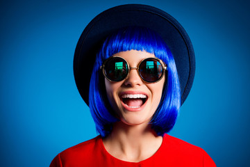 Head shot portrait of funny comic girl with beaming smile in headwear eyewear wig laughing laud isolated on blue background. Delight pleasure rest relax concept