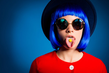 Portrait of childish stupid woman in eyewear head wear gesturing tongue out with small yellow candy...